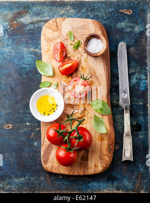 Geschnittene reife Tomaten auf Olivenholz-Schneidebrett auf blauem Hintergrund Stockfoto