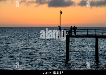 Fischer auf dem Pier sind Silhouette gegen den Sonnenuntergang bei Adelaide Brighton Beach, Australien Stockfoto