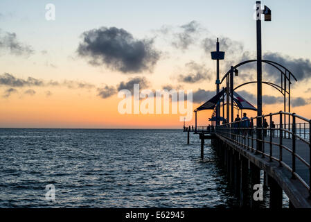 Angler und andere Leute, die auf dem Pier spazieren gehen, werden vom Sonnenuntergang am Brighton Beach, Südaustralien, abgeschirmt Stockfoto