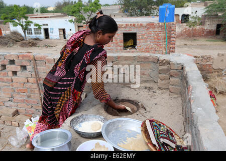 Frau in traditioneller Kleidung Roti Brot (bekannt als Chapati) in einem Lehmofen backen. Khushpur Dorf, Provinz Punjab, Pakistan Stockfoto