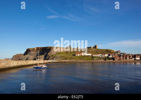 Ein kleines Boot Whitby Hafen mit dem historischen zerstörten Kloster oben auf den Klippen im Hintergrund verlassen. Stockfoto