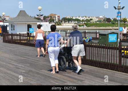 Zwei Leute Mann Frau schieben des Rollstuhls Clacton auf See Pier Sonne Sonnenschein Sommer Stockfoto