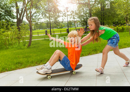 Mädchen treibt junge mit Arme auseinander auf skateboard Stockfoto