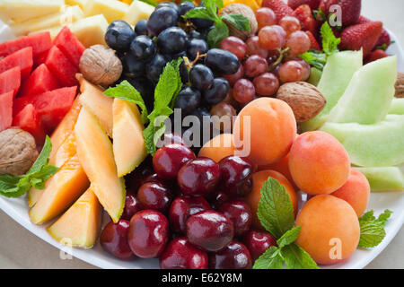 Bunte Sommer Obstteller mit Ananas, Wassermelone, Kirschen, Aprikosen, Erdbeeren, Melone, Walnüssen und Minze Stockfoto