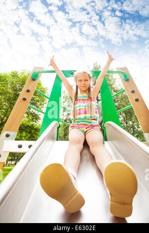 Mädchen mit Händen oben sitzt auf Spielplatz Rutsche Stockfoto