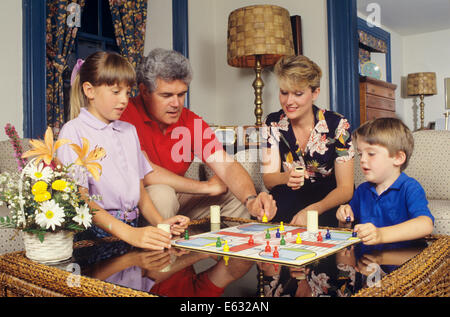 1980S 1990S ENGAGIERTE VIERKÖPFIGE FAMILIE BRETTSPIEL PARCHEESI ZU HAUSE IM WOHNZIMMER SITZEN Stockfoto