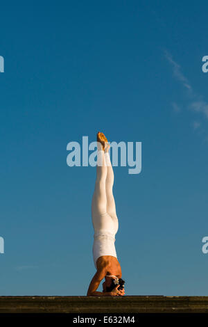 Junge Frau Hatha Yoga im Freien praktizieren, zeigt die Pose Sirshasana, Kopf stand Stockfoto