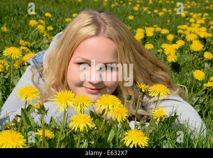 Lächelndes Mädchen, 15 Jahre, liegend in einem Feld von Löwenzahn, Schweden Stockfoto
