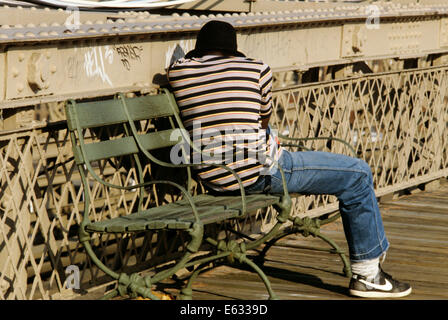 ANONYME JUNGE AFROAMERIKANISCHE MANN SITZEN AKTIVIERT ENTFERNT AUF EISENBRÜCKE BANK SCHLAFEN Stockfoto