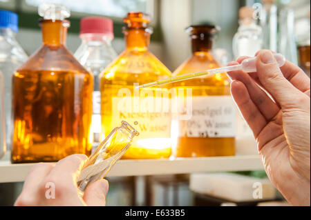 Ein Labor-Arbeiter mit einer Pipette auf eine chemische Flüssigkeit in einen Glasbehälter füllen Stockfoto