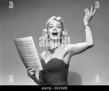 1950ER JAHRE BLONDE FRAU SINGEN HOLDING NOTEN TRAGEN TRÄGERLOSEN KLEID HALSKETTE Stockfoto