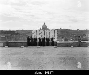 1950ER JAHREN ROM ITALIEN RÜCKANSICHT DER STUDENT PRIESTER AUFGEREIHT DURCH WAND MIT BLICK AUF STADT MIT BLICK AUF ST.-PETERS-BASILIKA IM HINTERGRUND Stockfoto