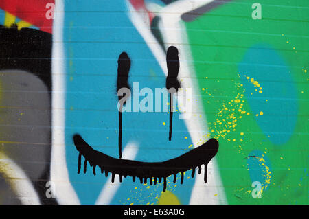 Abstrakt, lächelndes Gesicht an Wand mit bunten Graffiti und Spritzwasser Farbe. Stockfoto