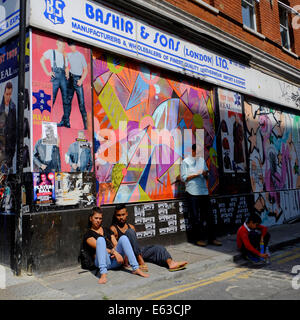 Menschen sitzen auf Pflaster gegen Wand an einem sonnigen Tag in Shoreditch Stockfoto