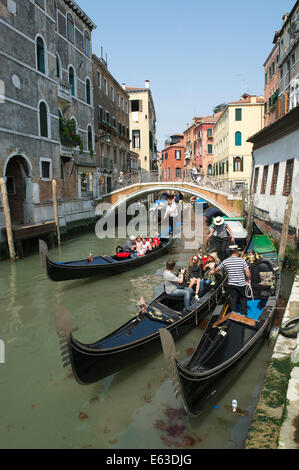 Venedig, Italien - APRIL 2013: Touristen Gondelfahrten passieren andere Gondeln mit Gondolieri auf einen kleinen Kanal. Stockfoto