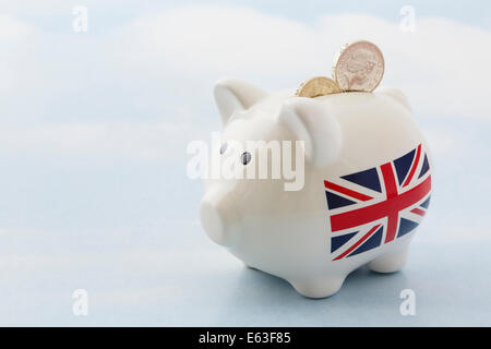 Sparschwein mit britischen Union Jack und zwei Pfund Sterling Pfund-Münzen in Slot auf einem blauen Himmelshintergrund, finanzielles Wachstum nach Austritt in UK Großbritannien Stockfoto