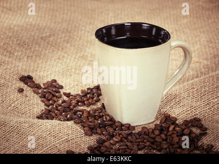 Tasse schwarzen Kaffee und Kaffeebohnen auf Sackleinen Hintergrund, geringe Schärfentiefe, Vintage Filtereffekte Stockfoto