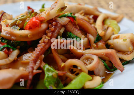 Nahaufnahme von gebratenen Tintenfisch und Basilikum auf weißen Teller und Bambus Korb Hintergrund weichzeichnen;  selektiven Fokus mit Unschärfe Zeitmessung Stockfoto