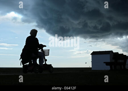 Gewitterwolken Brauen über Strandhütten und Boote an der Strandpromenade von Göring, West Sussex, wie Radfahrer und Menschen vorbeigehen Stockfoto