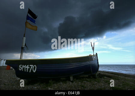 Gewitterwolken Brauen über Strandhütten und Boote an der Strandpromenade von Göring, West Sussex, wie Radfahrer und Menschen vorbeigehen Stockfoto