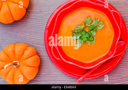 Eine Schüssel mit Kürbissuppe und ein paar rohe Mini Kürbisse auf einem Holztisch Stockfoto