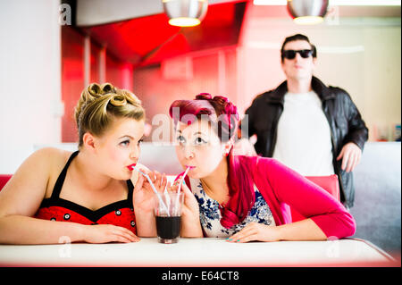 Zwei Frauen gekleidet im 50er Jahre Stil American Pin-up-Kleidermode ein Glas Coca-cola Coke in einem Diner UK teilen Stockfoto