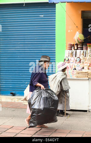 BANOS, ECUADOR - 28. Februar 2014: Unbekannte ältere Frau gehen barfuss Strasse Ambato tragen eine schwarze Plastiktüte Stockfoto