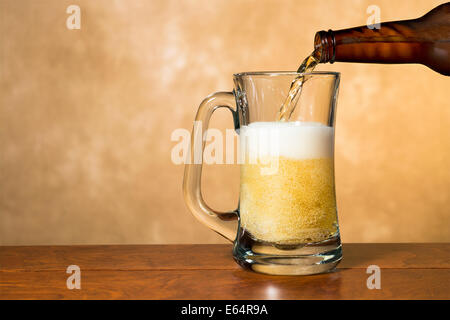 Frische, kalte, frische Bier in einen klassischen Pint Becher gegen eine fleckige Goldgrund gegossen wird. Stockfoto