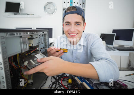 Lächelnde Informatiker arbeiten an defekten Konsole mit Schraubendreher Stockfoto