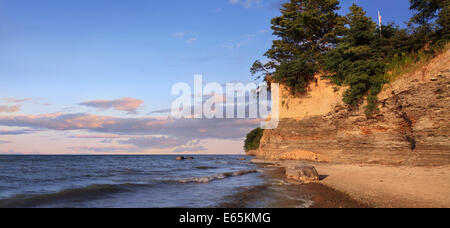 Ein Findling sitzt In der Brandung mit Klippen hinter strahlenden Morgenlicht, Erie-See am Strand von Barcelona, New York, USA Stockfoto