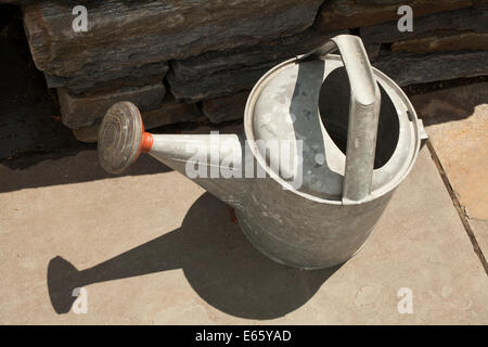 Verzinktes Metall Gießkanne sitzt auf einer Steinplatte Terrasse. Stockfoto