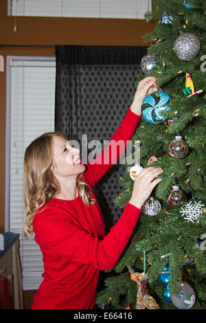 Eine junge blonde hübsche Frau in einem roten Pullover, einen Weihnachtsbaum zu schmücken. Stockfoto