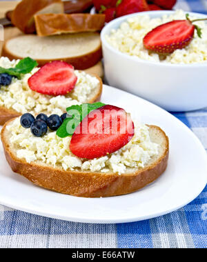 Scheiben Brot mit Quark-Creme, Heidelbeeren und Erdbeeren, Minze, eine Schüssel mit Quark, Brot auf einem Brett auf einem Hintergrund Stockfoto