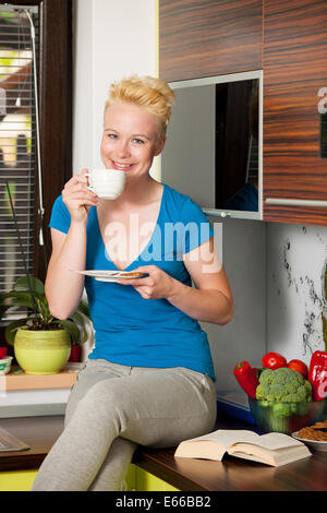 Schöne junge kaukasischen blonde Frau trinken Kaffee in der Küche im Cosy home Stockfoto