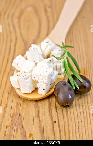 Feta-Käse in einem Holzlöffel, schwarzen Oliven und Rosmarin auf Holzbrettern Hintergrund Stockfoto
