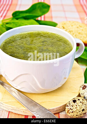 Suppe von grünen Brennnesseln, Sauerampfer, Spinat, Rhabarber Blätter auf einem runden Holzbrett, Brot, Wachteleier, Löffel auf einem Tuch-Hintergrund Stockfoto