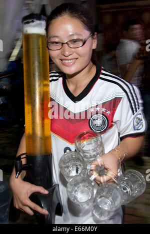 Qingdao, China. 16. August 2014. Eine Kellnerin trägt ein Fußball-Team-Trikot während des Tragens Bier und Bierkrüge 24. Oktoberfest in Qingdao, China, 16. August 2014. Laut Veranstalter ist es zum größten Volksfest in Asien. Foto: FRISO GENTSCH/Dpa/Alamy Live News Stockfoto