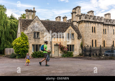 Mann/Vater und Kind, wandern vorbei an alten Haus neben Cecily Hill Kaserne (faux mittelalterlichen Burg), Cirencester Park Eingang, Cotswolds, England, UK. Stockfoto