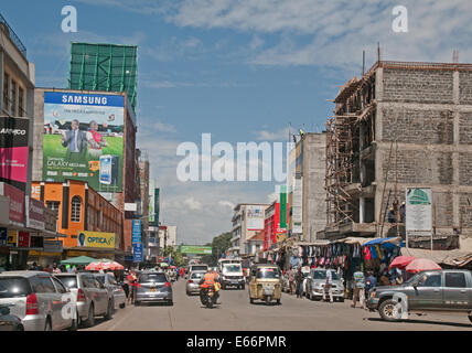 Menschen und Verkehr auf Kenyatta Avenue Nakuru Kenia in Ostafrika mit Werbung Werbetafeln Geschäften und Piaggio Ape 3-Rad-taxi Stockfoto