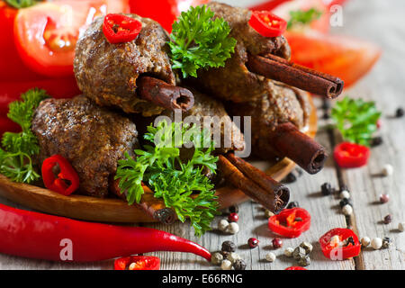 Traditionelles Lamm Kebab auf Zimt-sticks auf Holzplatte mit roten Paprika, Tomaten und Petersilie. Selektiven Fokus. Stockfoto