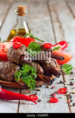 Traditionelles Lamm Kebab auf Zimt-sticks auf Holzplatte mit roten Paprika, Tomaten und Petersilie. Selektiven Fokus. Stockfoto