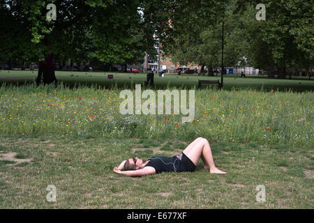 Hackney - London Fields. Wildblumenwiese. Junge Frau auf dem Rasen liegen, entspannen und Musik hören. Stockfoto