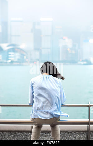 Mädchen sitzen auf einem windigen Tsim Sha Tsui Promenade mit Blick auf Victoria Harbour, Hongkong Stockfoto