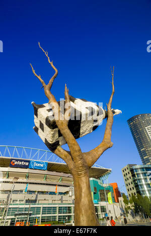 Kuh auf einen Baum auf den Kopf nach unten schwarz & weiße Kuh Skulptur vor tiefblauem Himmel, Telstra Dome im Hintergrund Docklands, Melbourne Stockfoto
