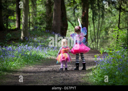 Zwei Mädchen im Märchen Kleider zu Fuß durch eine englische Bluebell Holz im Frühjahr. Stockfoto