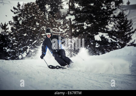 Skifahrer tragen einen schwarzen Helm mit einer Helmkamera und Brille wirft eine Wolke aus Schnee wie er auf der Piste beschleunigt. Stockfoto
