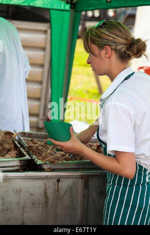 Lauch & Bezirk SHOW, Lauch, STAFFORDSHIRE, ENGLAND A Young Woman in grüne Schürze Portion gezogen Schweinefleisch aus einer Garküche. Stockfoto