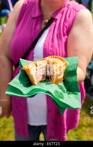 Lauch & Bezirk SHOW, Lauch, STAFFORDSHIRE, ENGLAND A Young Woman hielt ein Pork Pie auf grünem Papier Serviette zu teilen. Stockfoto