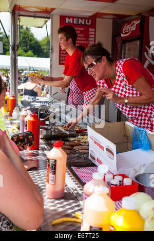 Lauch & Bezirk SHOW, Lauch, STAFFORDSHIRE, ENGLAND A Frau trägt rot karierte Schürze mit einer heißen Speisen aus einer Burger-stand Stockfoto