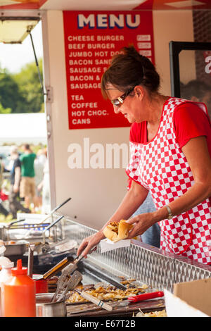 Lauch & Bezirk SHOW, Lauch, STAFFORDSHIRE, ENGLAND A Frau trägt rot karierte Schürze dient einen Hot Dog von einem Burger-stand Stockfoto